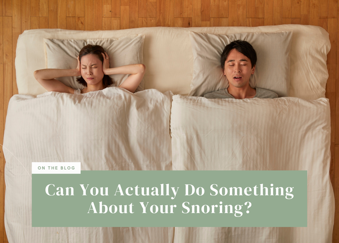Overhead view of a woman covering her ears in bed next to a snoring partner.