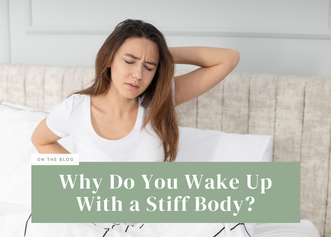Woman sitting up in bed wincing while holding her lower back and neck.