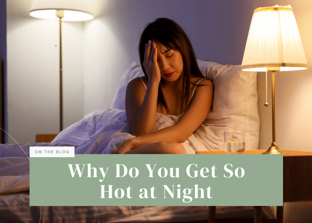 Woman sitting up in bed under warm lamp light holding her hand to her head in discomfort.
