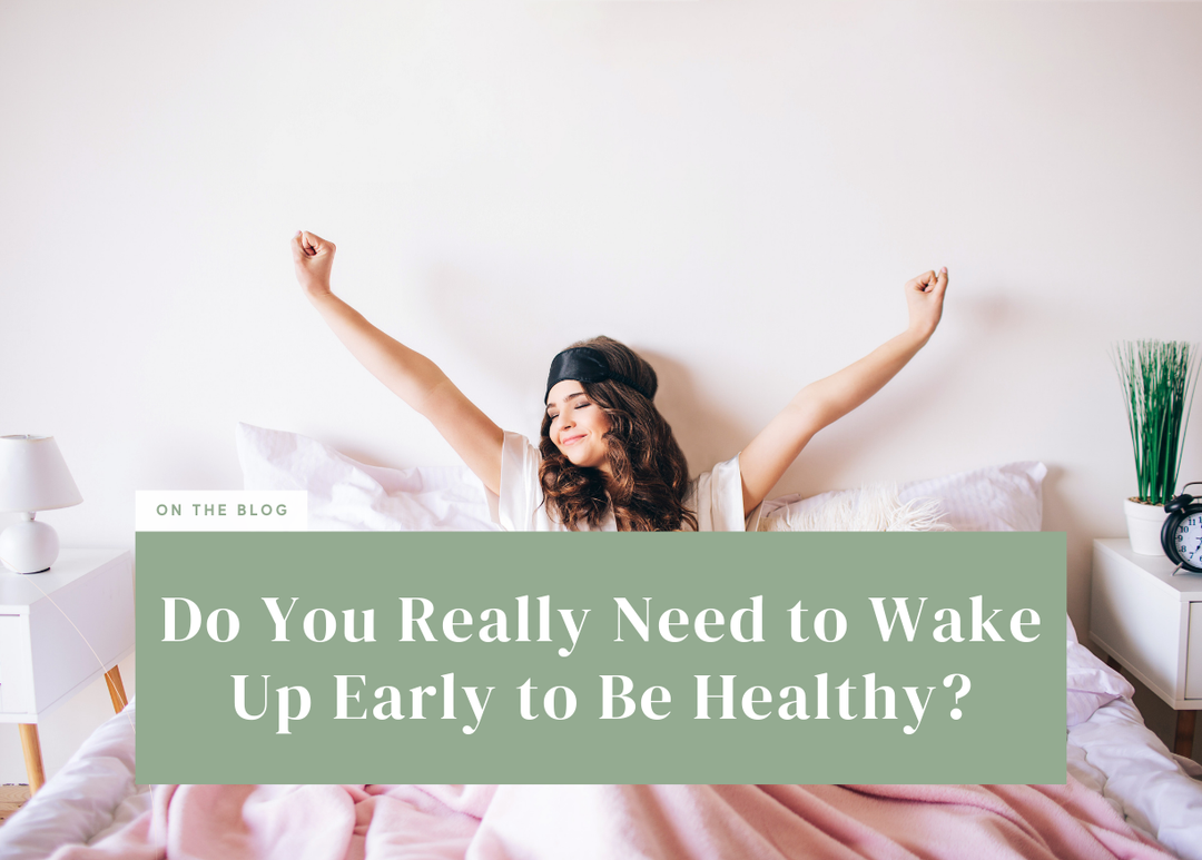Woman wearing a sleep mask waking up in bed with her arms stretched overhead.