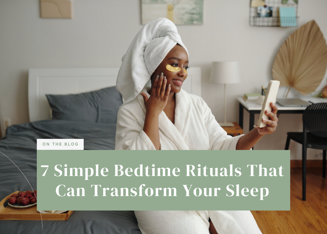 Woman in a white bathrobe and head towel applying skincare while sitting on the edge of a bed.