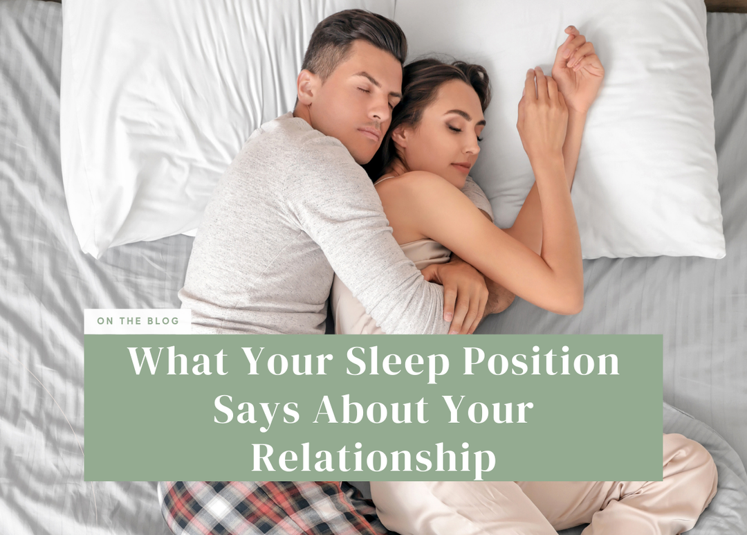 Overhead view of a couple spooning comfortably in bed under white pillows and grey sheets.