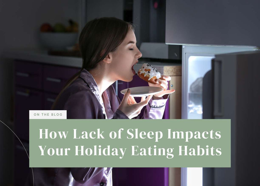 Woman wearing satin pajamas standing in front of an open refrigerator at night taking a bite out of a frosted donut.