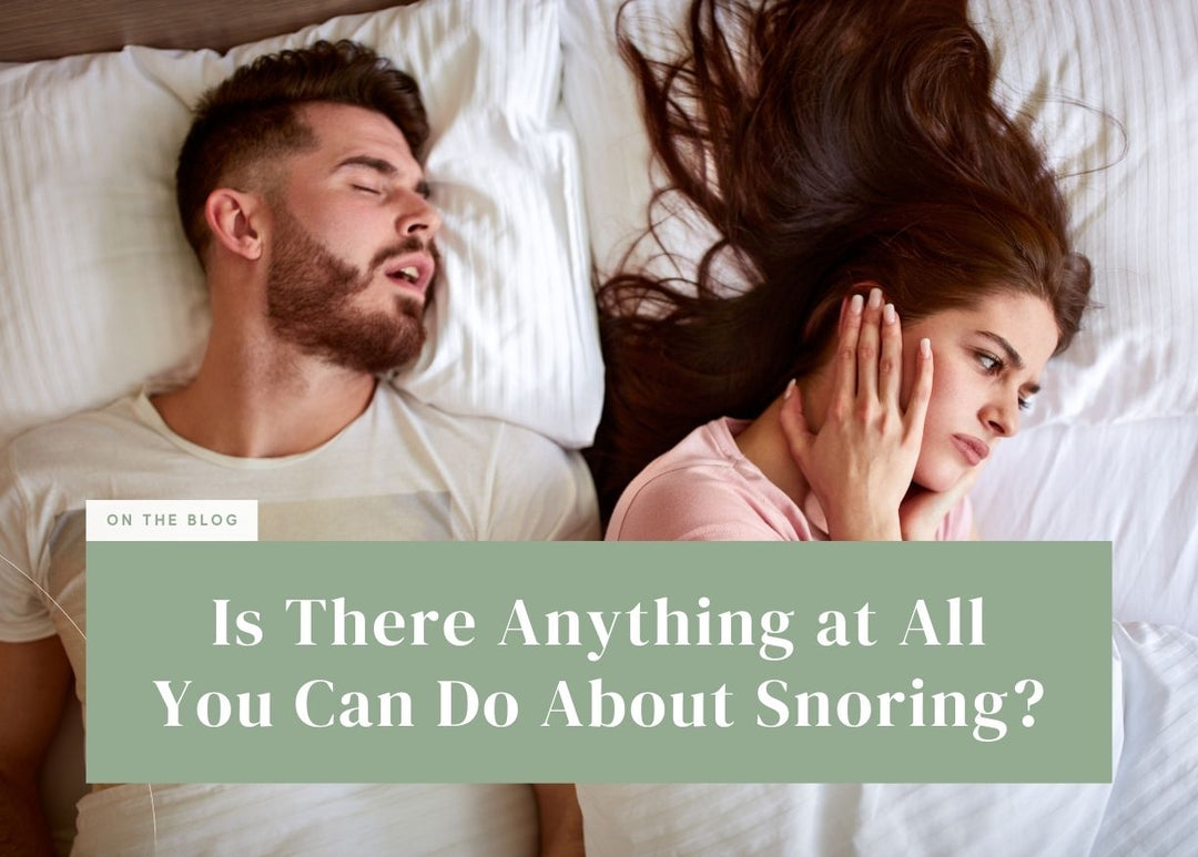 Frustrated woman covering her ear next to a man snoring in bed.