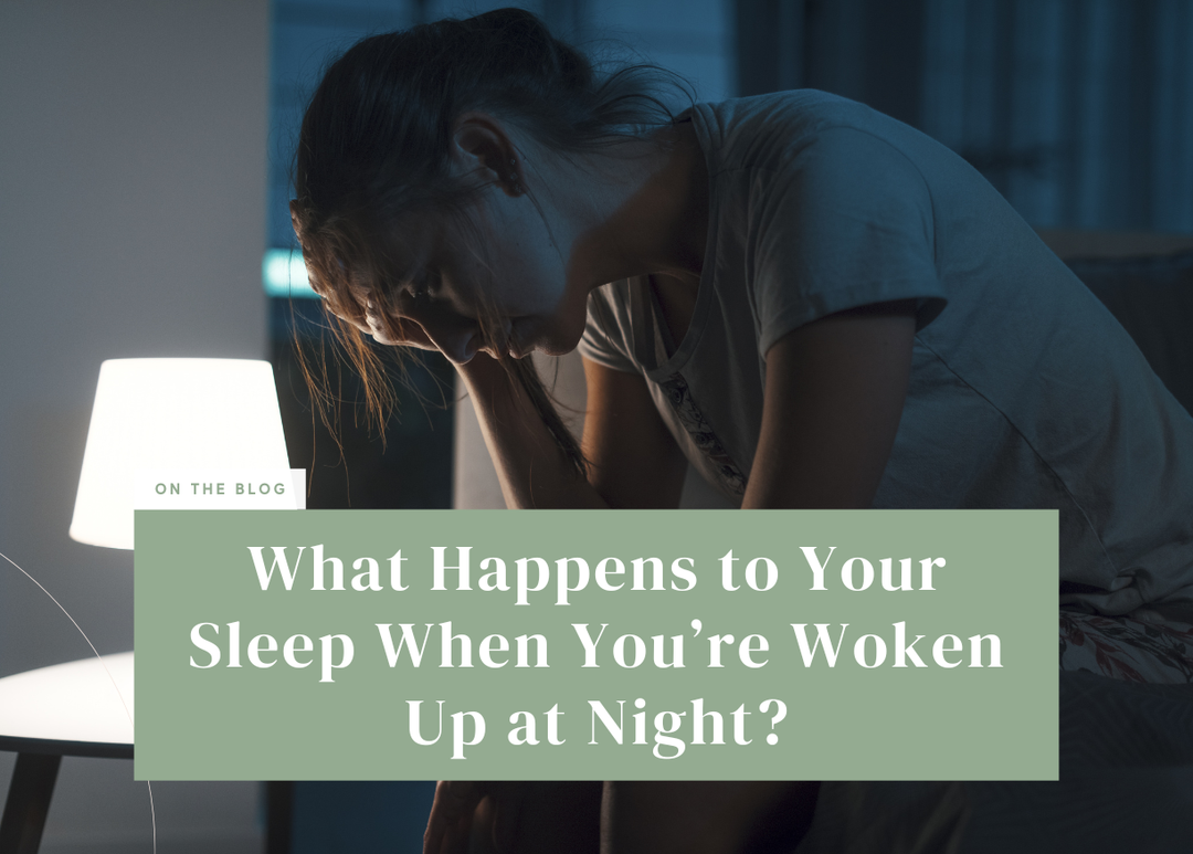 Woman sitting on the edge of a bed holding her head in her hands next to a lit nightstand lamp.